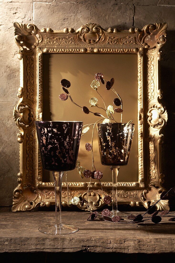 Two purple, stemmed glasses in front of a gilt mirror