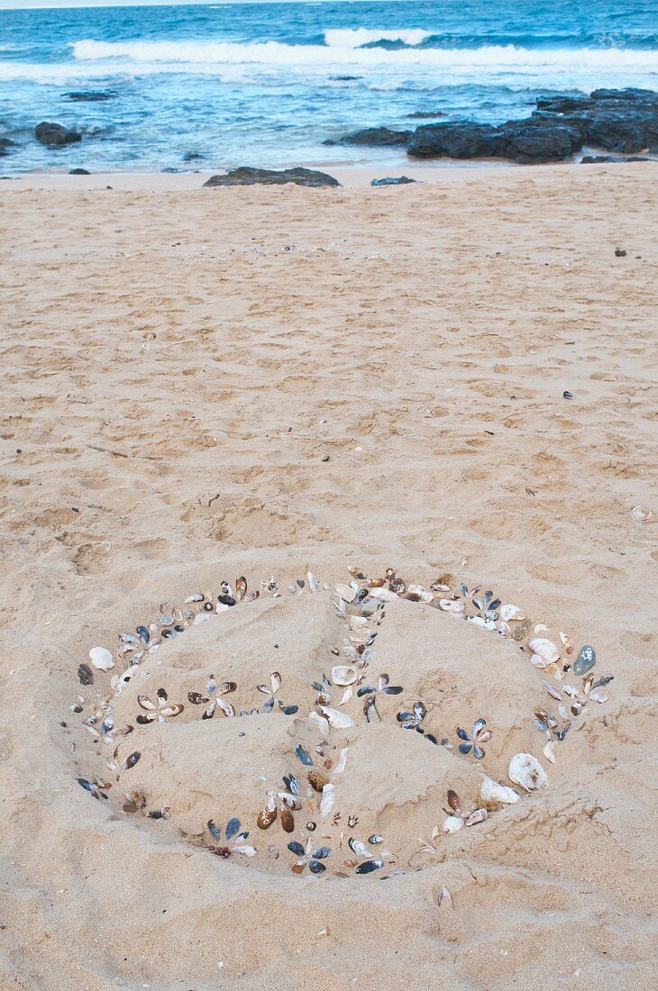 Peace - Zeichen aus Steinchen und Muscheln auf Sandboden