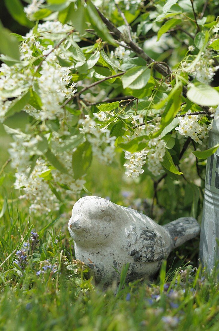 Stone bird figurine beneath lilac bush