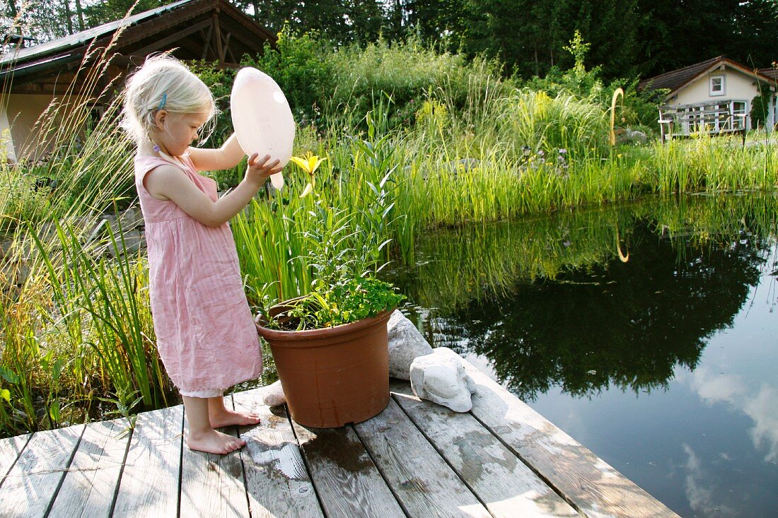 Blonde girl watering potted plant next to garden pond