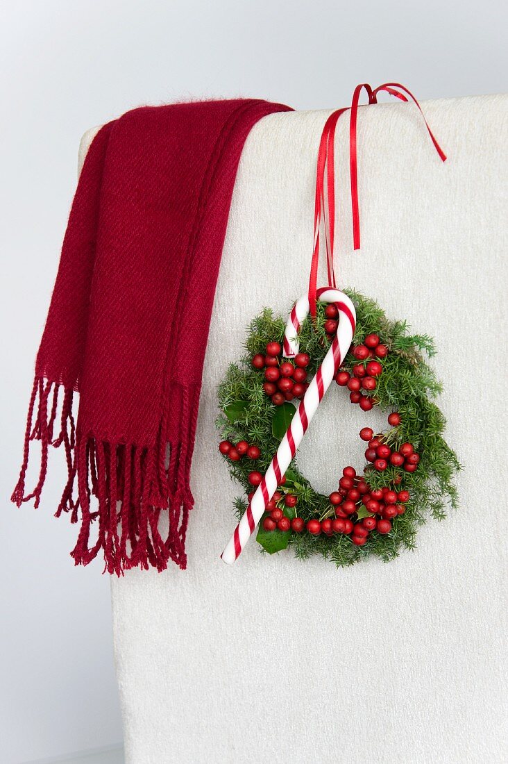 Christmas wreath of holly berries and conifer hanging on chair back with candy cane