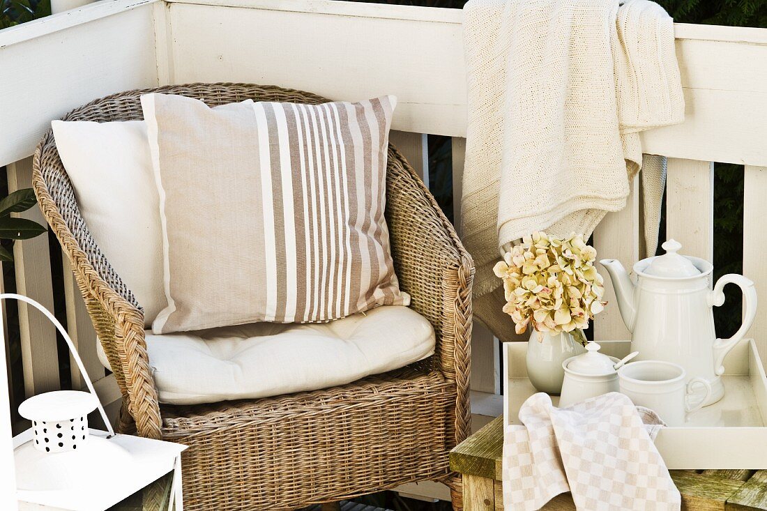 Nachmittagspause auf Veranda - Rattansessel mit Kissen neben Teeservice auf Beistelltisch