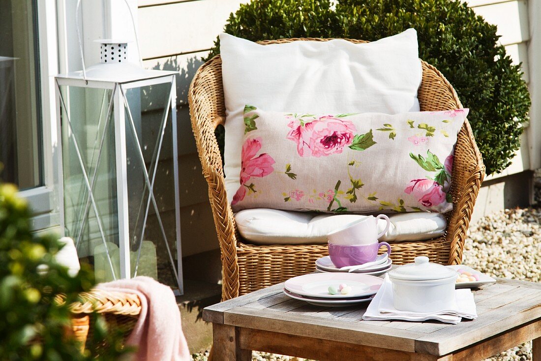 Kaffeepause im Freien - Rattanstuhl mit Kissen und Tassen auf Beistelltisch vor Hauswand
