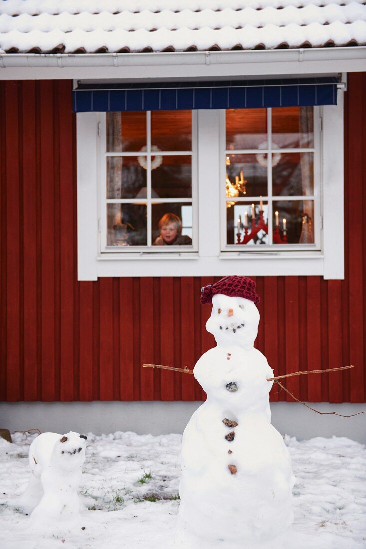 Junge schaut auf Schneemann vor dem Haus