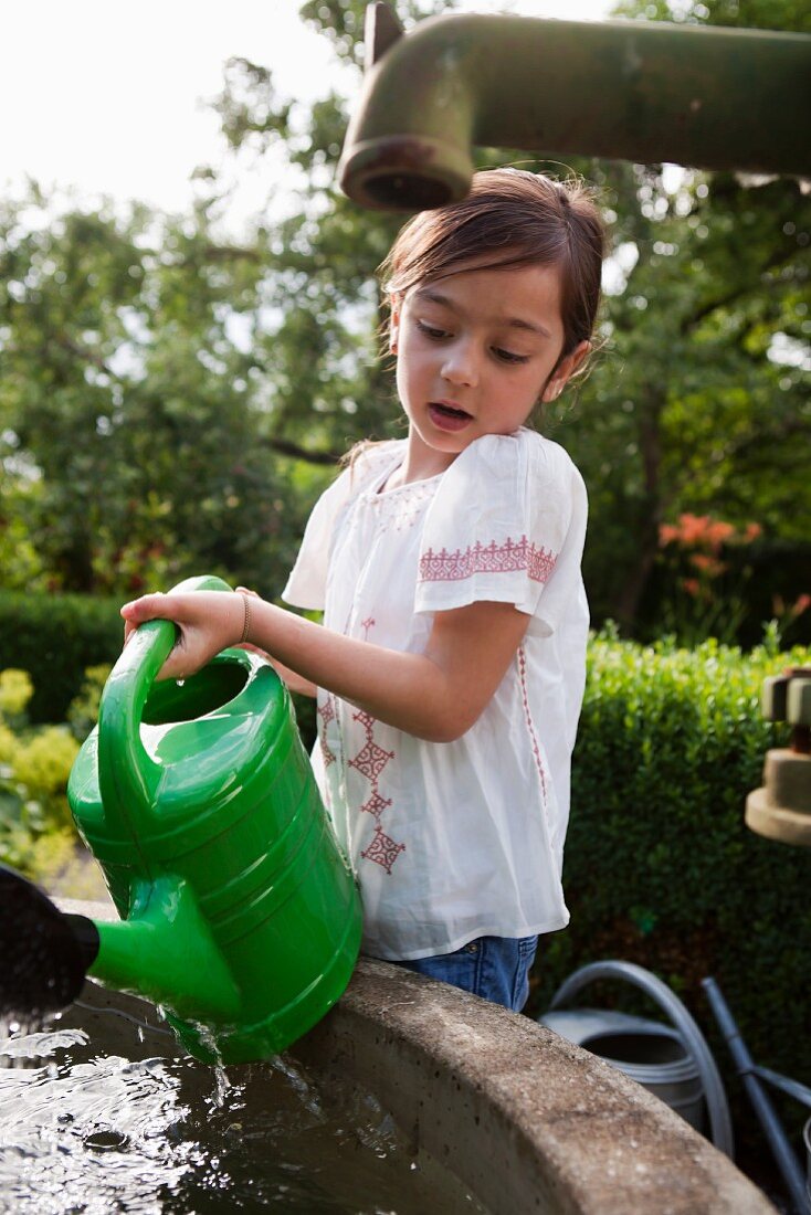Little girl filling watering can from well