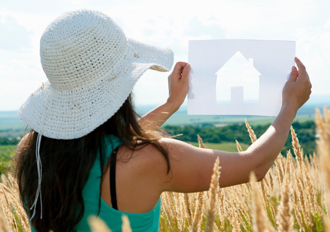 Woman holding up cut-out paper silhouette of house against landscape