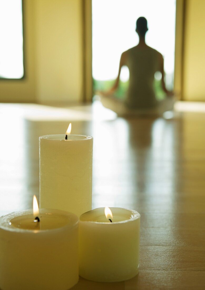 Yoga class, candles burning while person sits in lotus position in blurred background