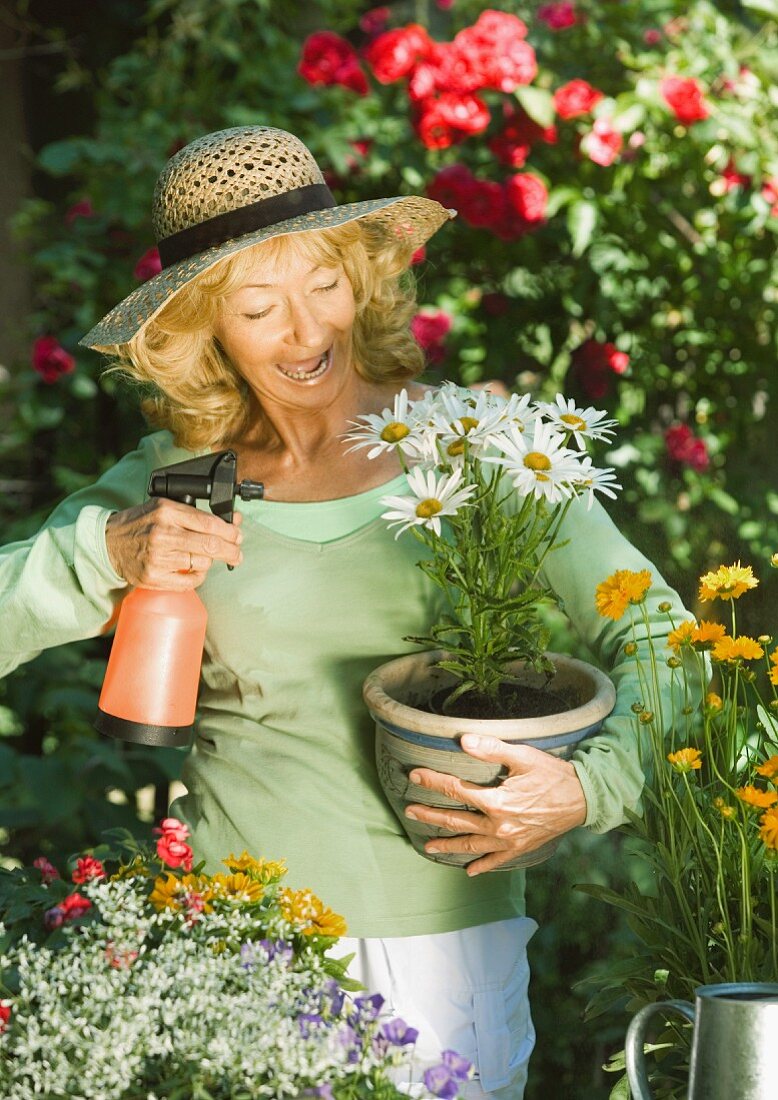 Frau im Garten mit Wasserbestäuber und Blumentopf