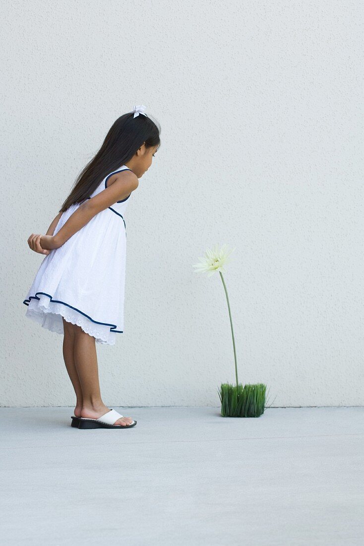 Kind steht vor einer Kunstblume auf dem Boden
