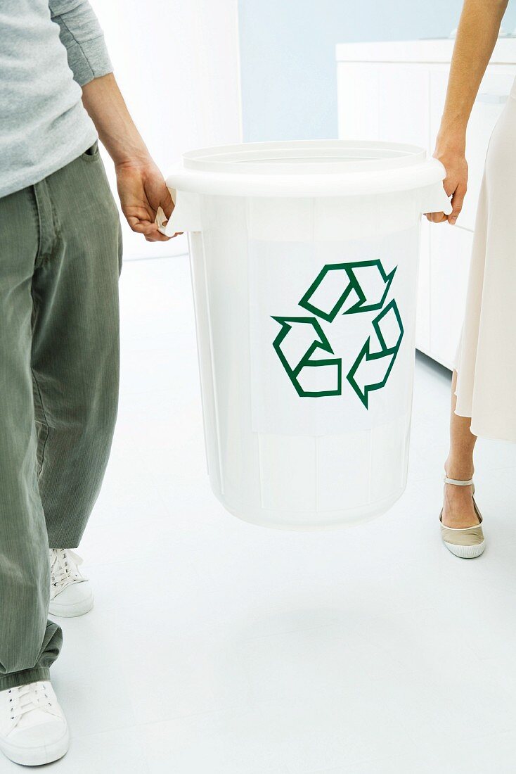 Two people carrying recycling bin together, cropped view