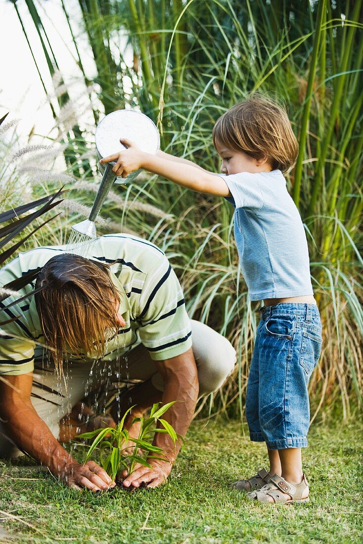 Little boy pouring water on his father's head as he works in garden