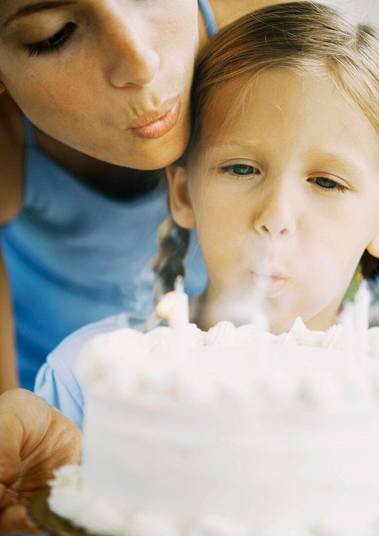 Mutter und Kind blasen Kerzen auf Geburtstagstorte aus