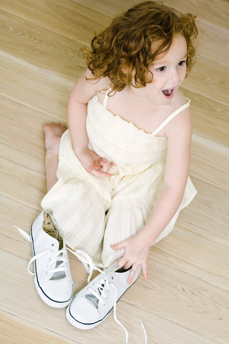 Little girl kneeling on ground near pair of shoes, looking surprised