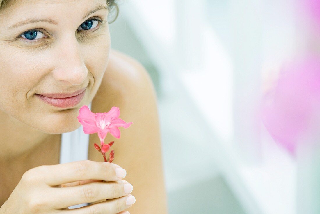 Woman smelling flower, smiling at camera, cropped