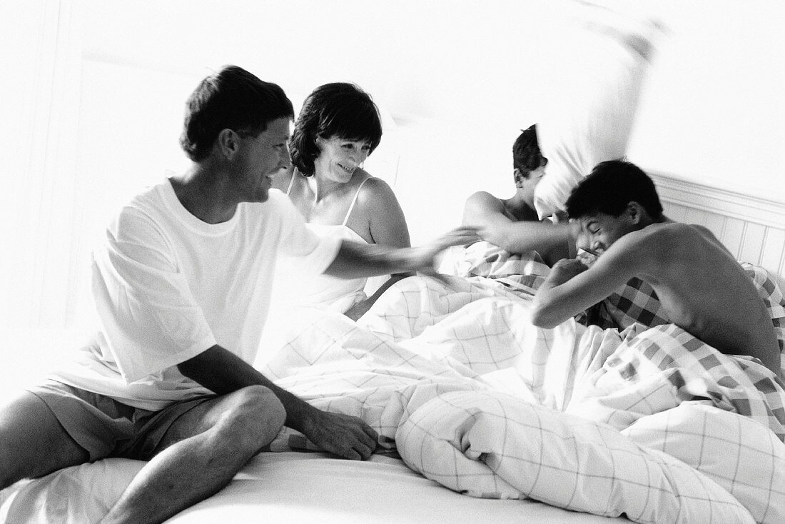 Family having pillow fight in bed, black and white
