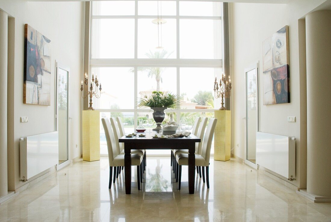 Dunkler Holztisch und weiße gepolsterte Stühle vor raumhohem Fenster in elegantem Ambiente