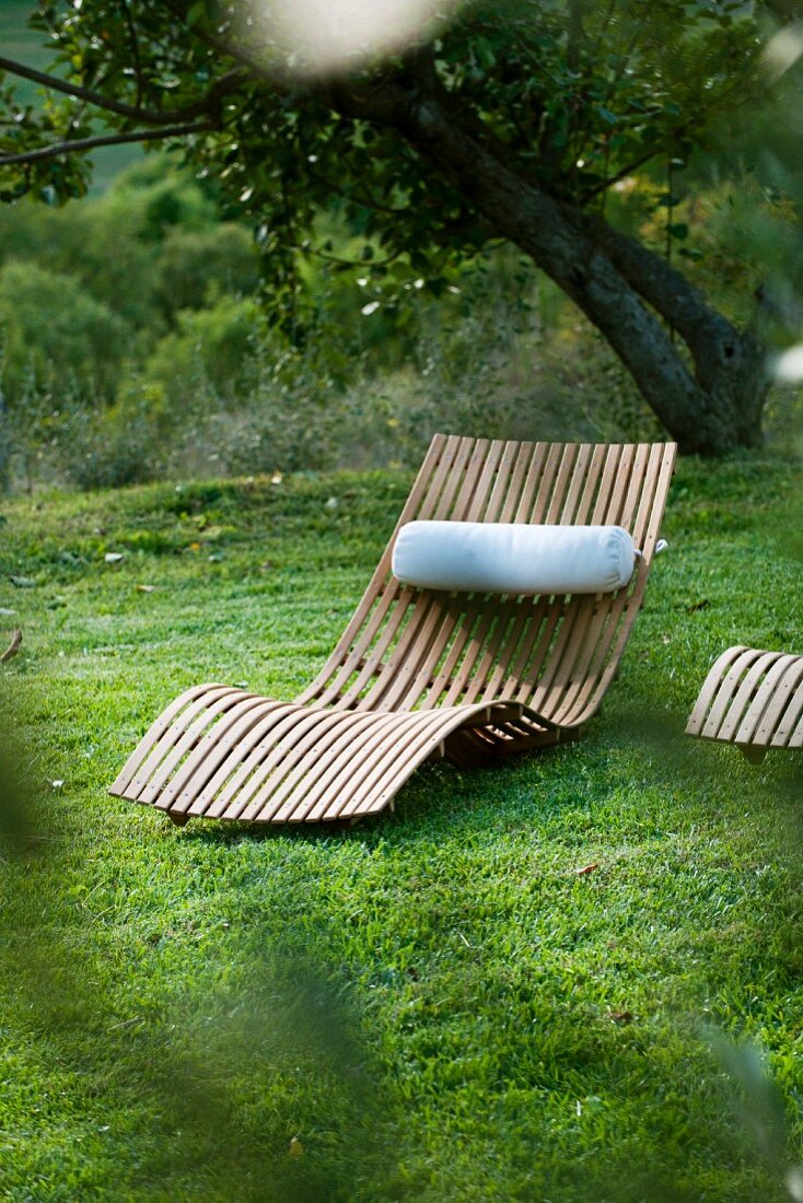 Sun lounger made of curved wooden slats with neck cushion in garden