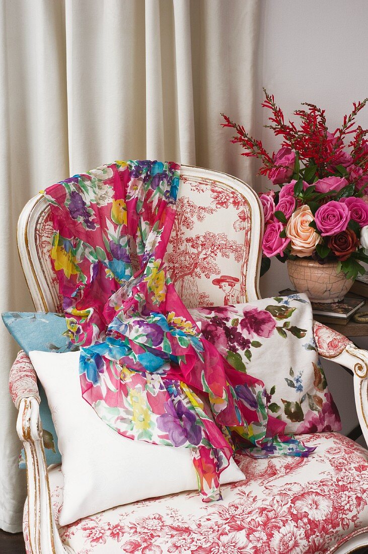 Colourful scarf on Rococo-style armchair next to flower arrangement