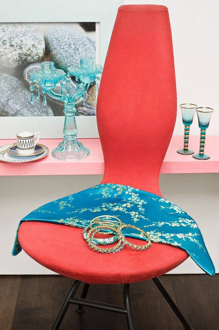 Modern chair decorated with bangles and silk scarf in front of glassware on shelf