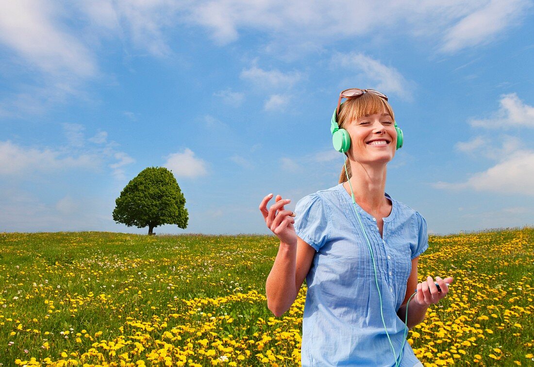 Woman listening to music through earphones in a meadow of dandelions