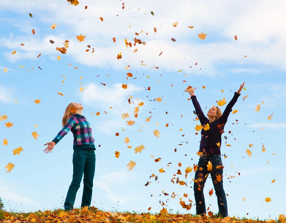 Mutter und Tochter werfen Herbstblätter in die Luft