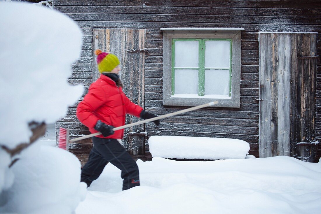 Mann mit Besen vor verschneitem Holzhaus