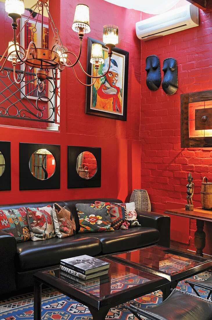 Wohnzimmerecke mit rot gestrichener Ziegelwand und afrikanische Kunst über Ledersofa