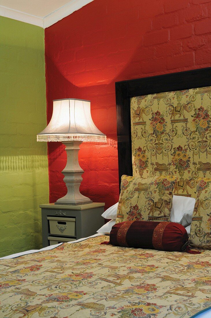 Large bedside lamp next to French bed with upholstered headboard in bedroom with green and red walls