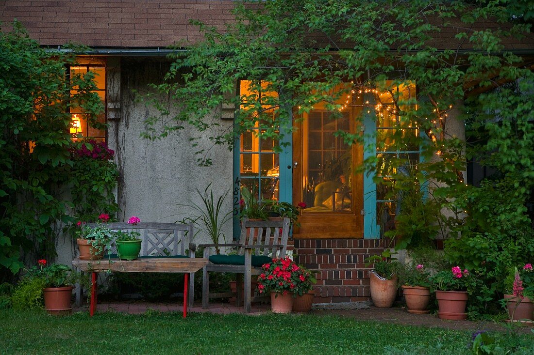 Verwunschenes Sitzplätzchen mit Ziegelstufen zur offenen Terrassentür und Blick in beleuchteten Wohnraum