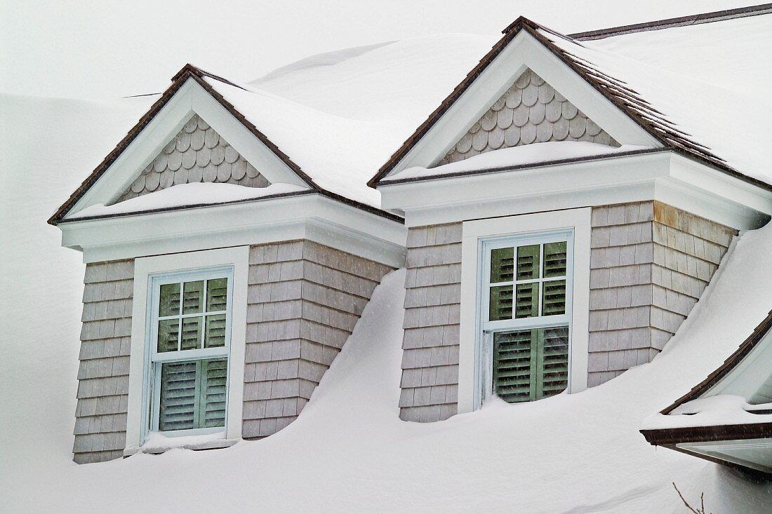 Mit Holzschindeln verkleidete Gauben in schneebedeckter Dachfläche