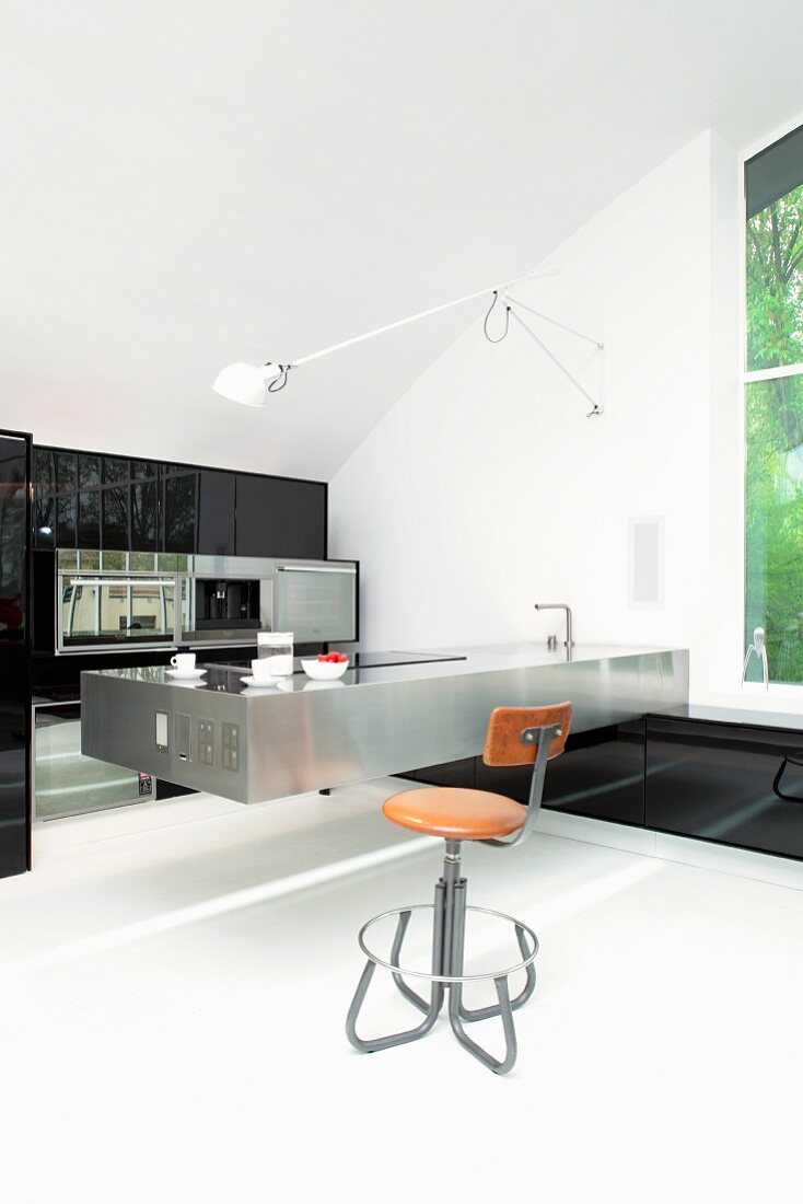 Retro barstool at stainless steel kitchen counter in minimalist kitchen with black fitted cupboards