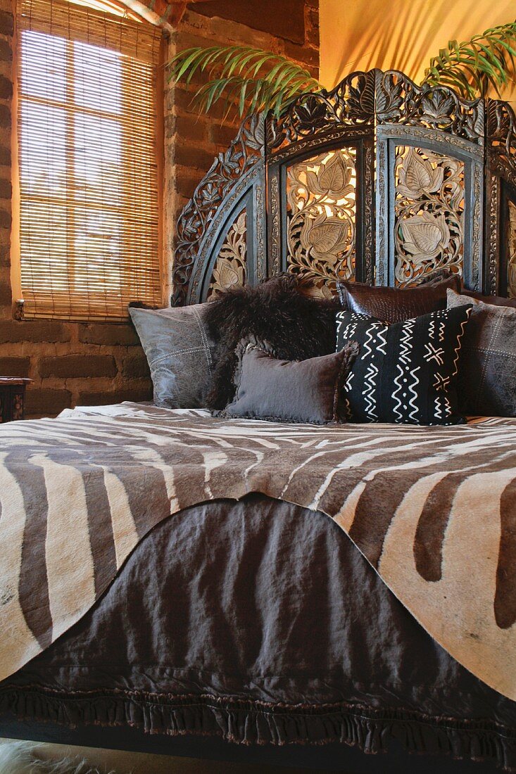 Tierfell und dunkle Bettwäsche auf Doppelbett mit geschnitztem Kopfteil