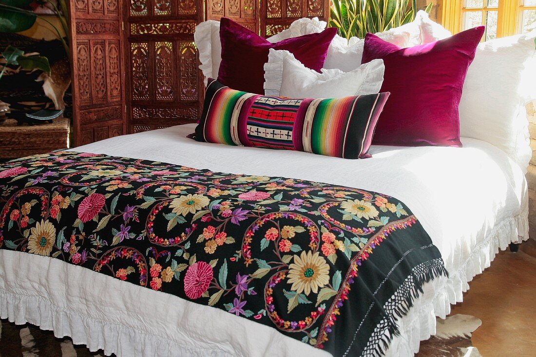 Bett mit folkloristischer Tagesdecke und verschiedenen Kissen in afrikanischem Stil
