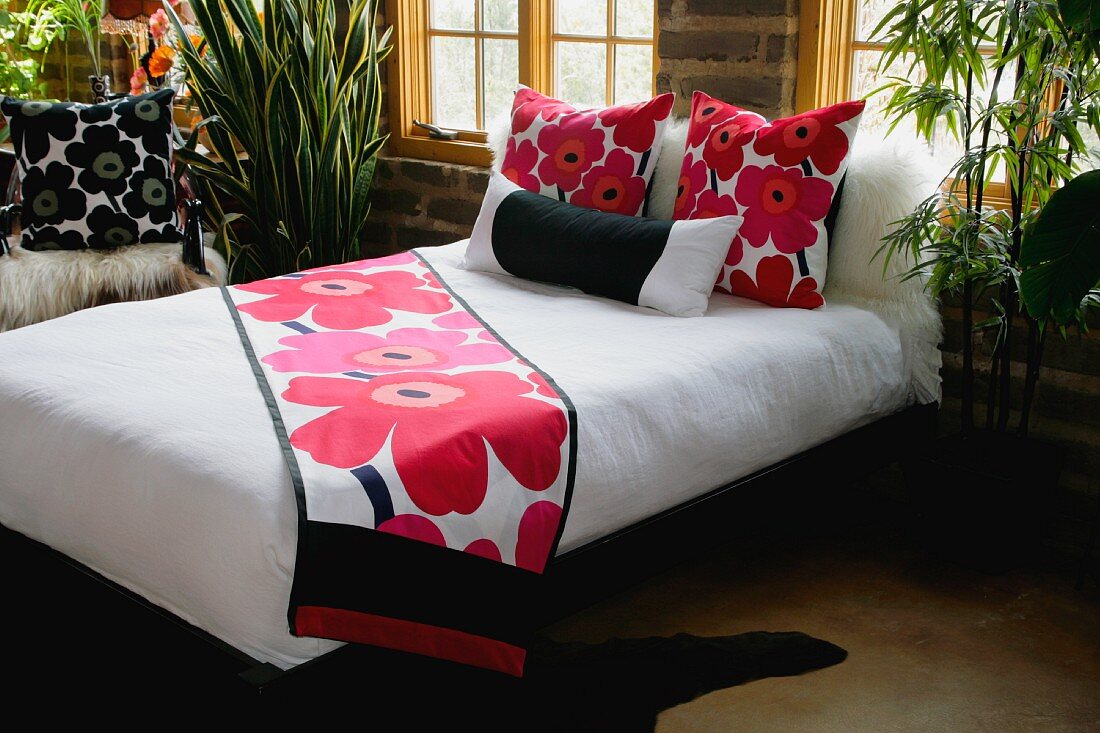 Doppelbett mit weisser Tagesdecke und modernem Blumenmuster auf Läufer und Kissen