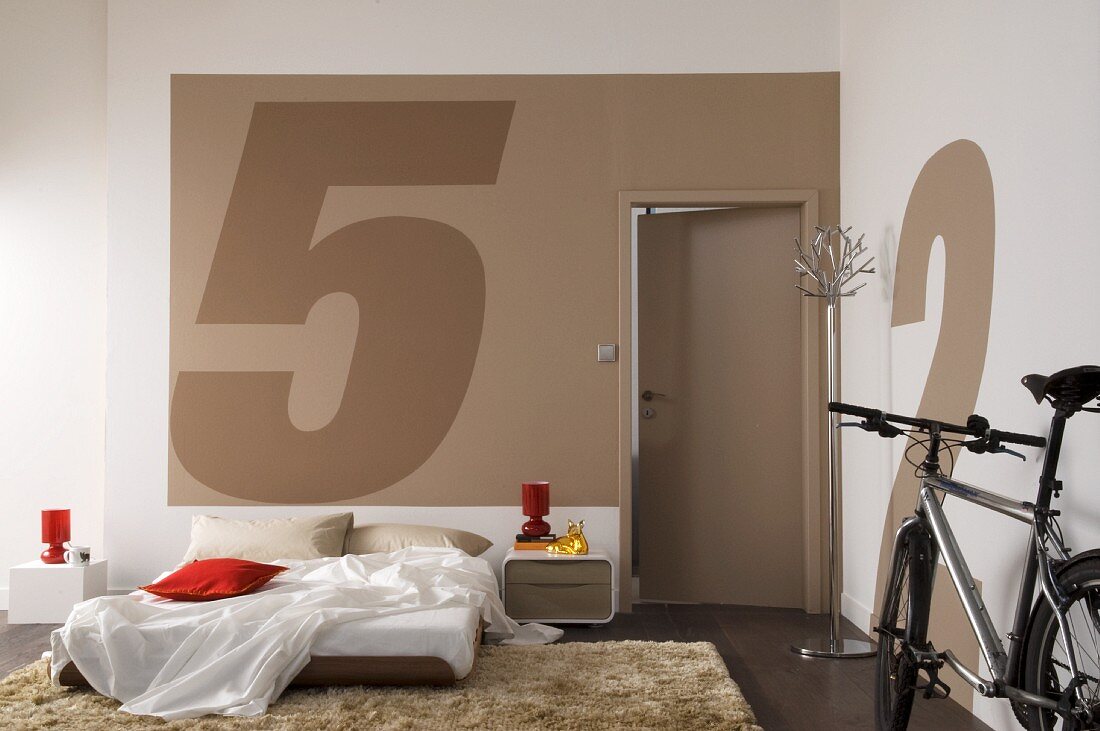 Modernes Schlafzimmer mit Bett auf Boden und geparktes Fahrrad vor Wand mit grossen, gemalten Zahlen