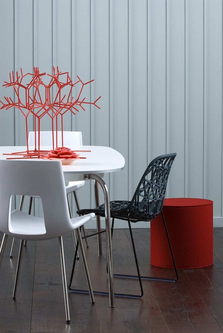 Stilisiertes Korallen Deko auf Tisch und moderne Stühle vor weisser Holzwand