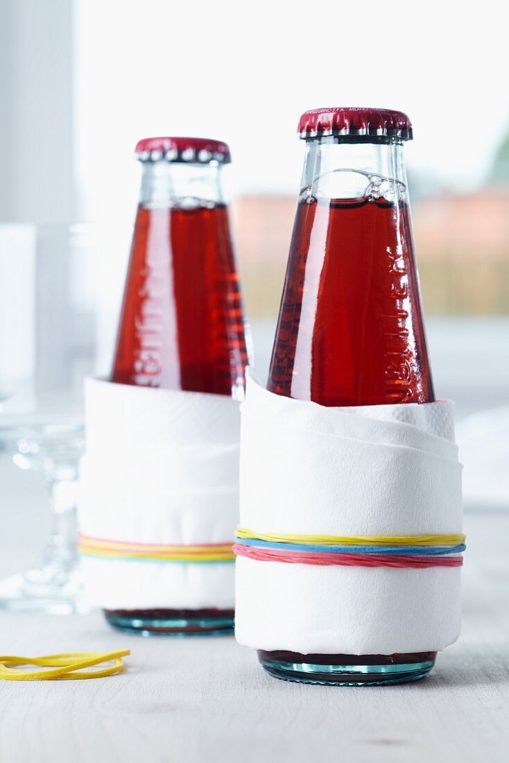 Tropfschutz für Trinkflaschen: Papierservietten mit Gummibändern befestigt