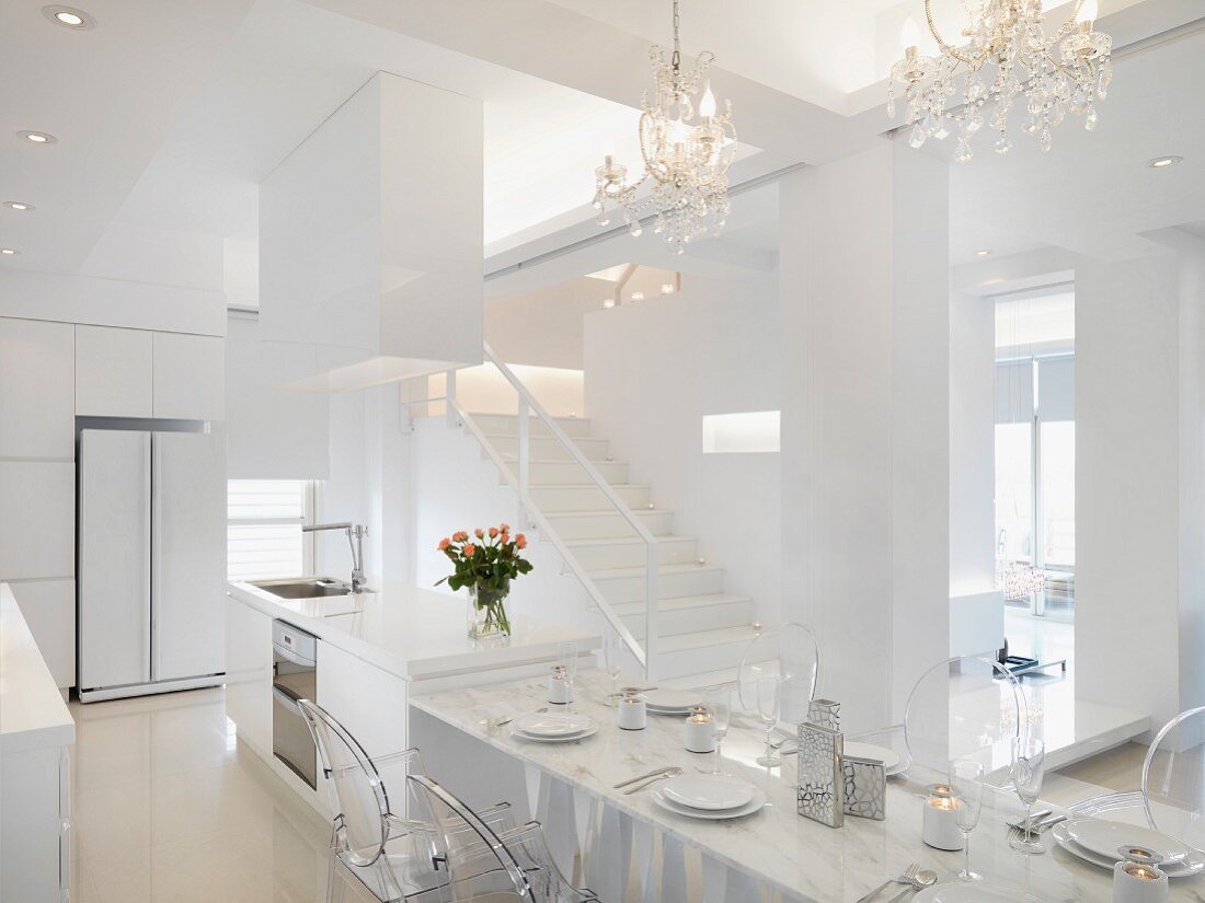 Minimalistischer, offener Wohnraum in Weiß mit Treppenaufgang und gedecktem Esstisch unter Kerzenleuchtern