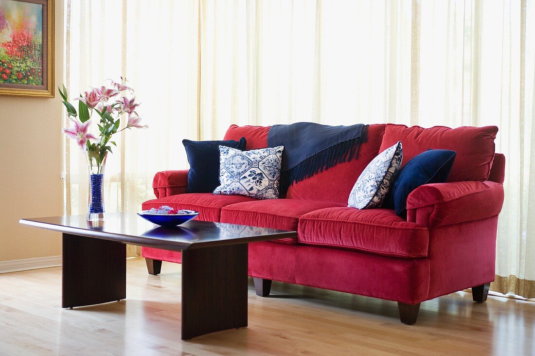 Pinkfarbenes Sofa mit Kissen und Couchtisch aus dunklem Holz vor geschlossenem Vorhang