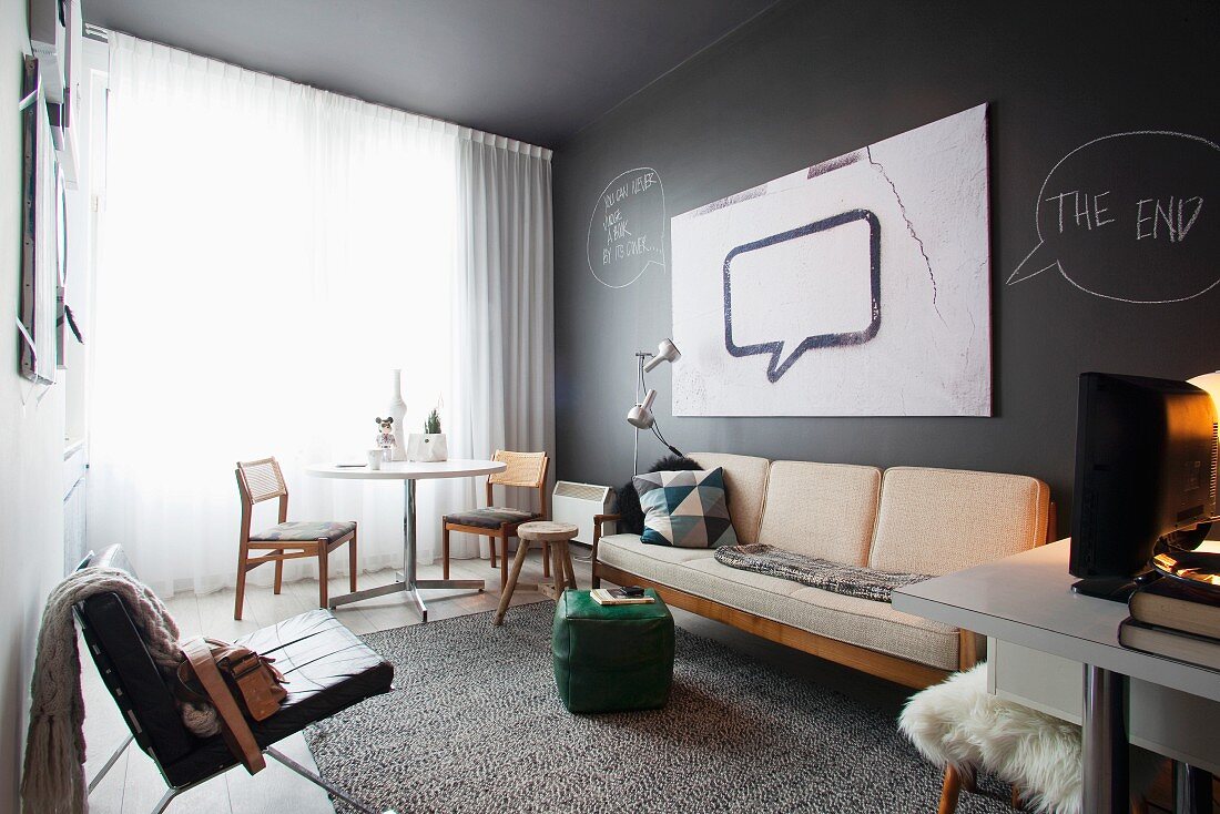 Moderner Wohnraum mit schwarzem Ledersessel gegenüber schlichter Sitzbank mit Polstern an schwarzer Wand und Essplatz am Fenster