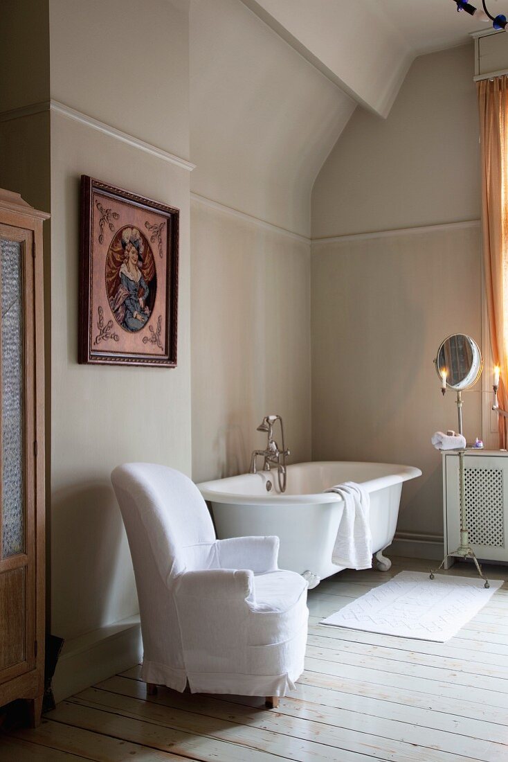 Armchair with loose white cover next to vintage bathtub in simple bathroom with traditional ambiance