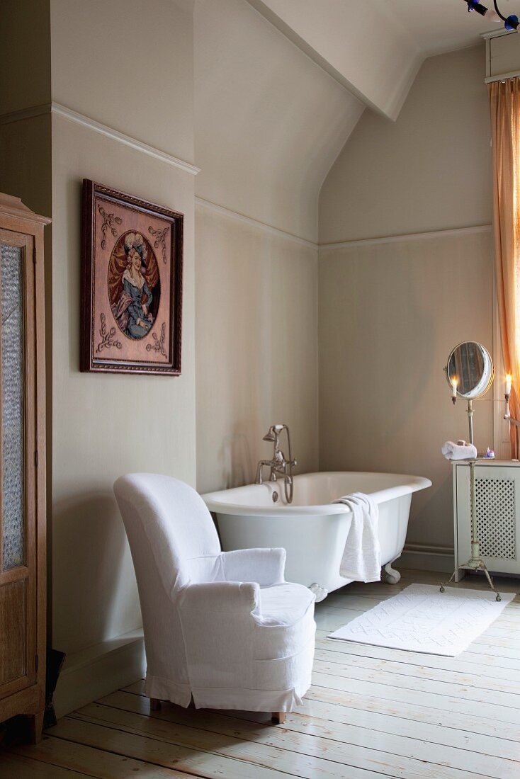 Sessel mit weisser Husse neben Vintage Badewanne in schlichtem Bad mit traditionellem Flair