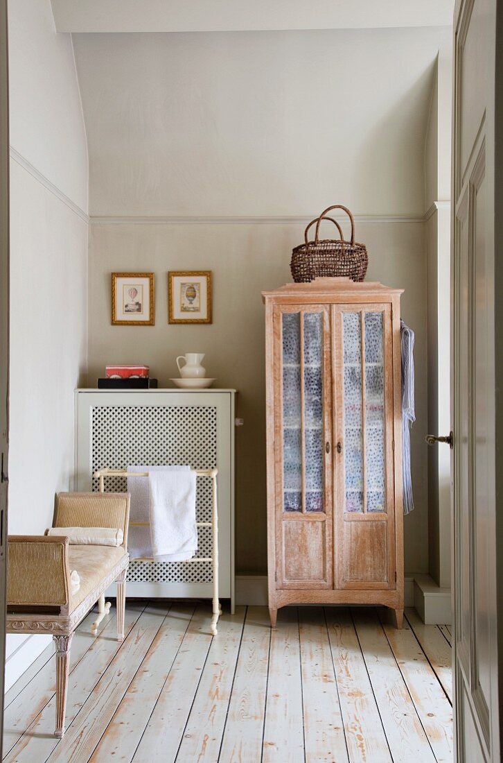 Rustic, antique cupboard with lattice doors and wood-clad radiator on old board floor in simple room