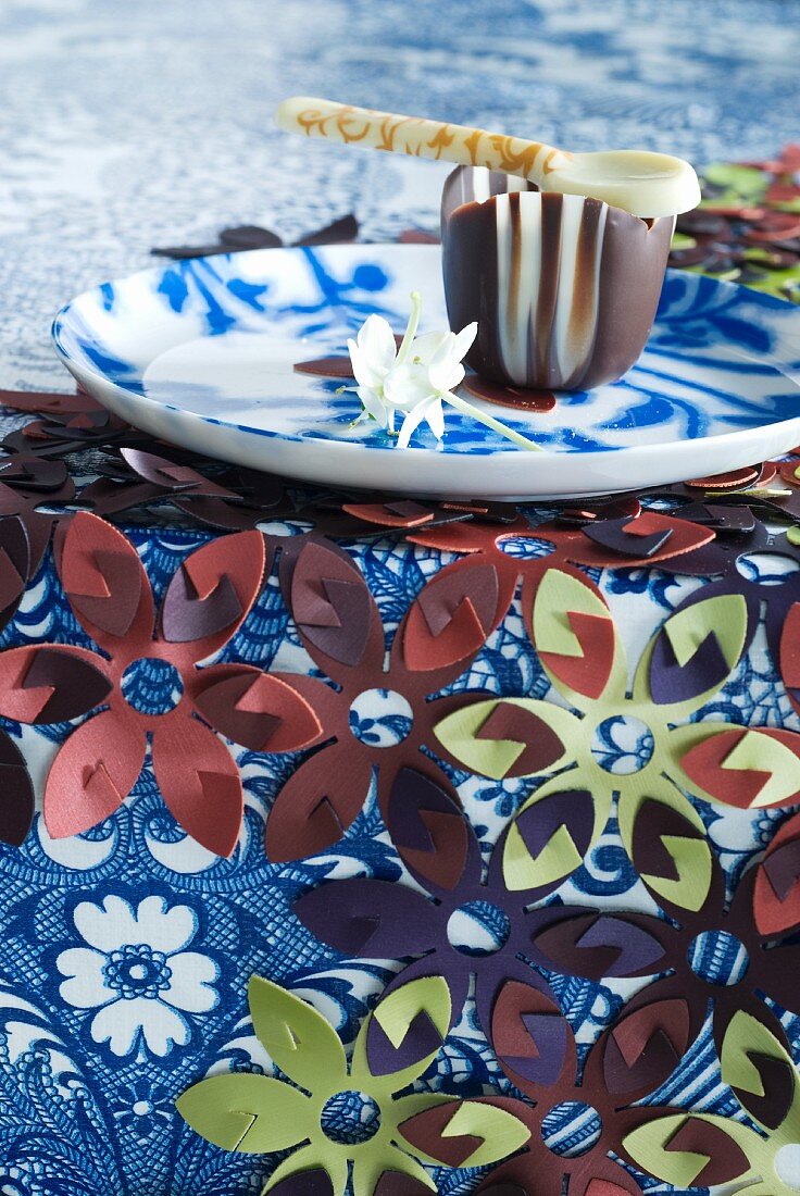 Tischdecke aus einzelnen Kunststoffblumen, und Teller mit Schokoschälchen und Schokolöffel
