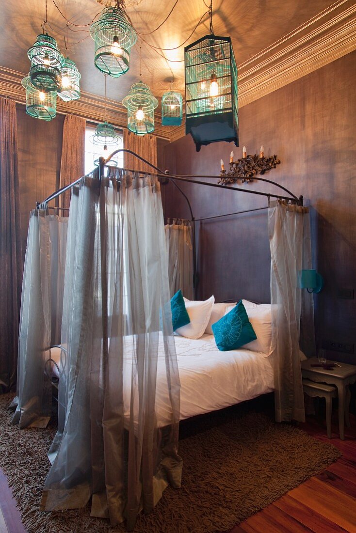 Himmelbett mit luftigen Vorhängen in herrschaftlichem Schlafzimmer und abgehängte Vogelkäfige als Deckenleuchten