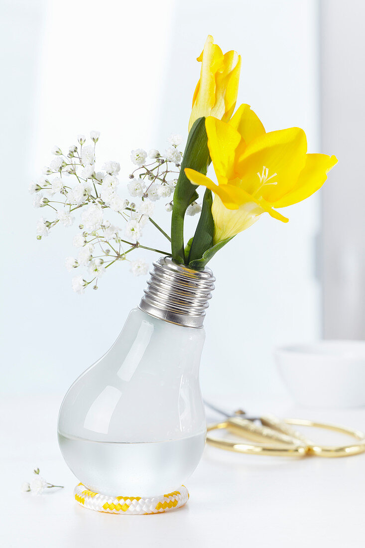 Light bulb used as vase holding freesias and gypsophila
