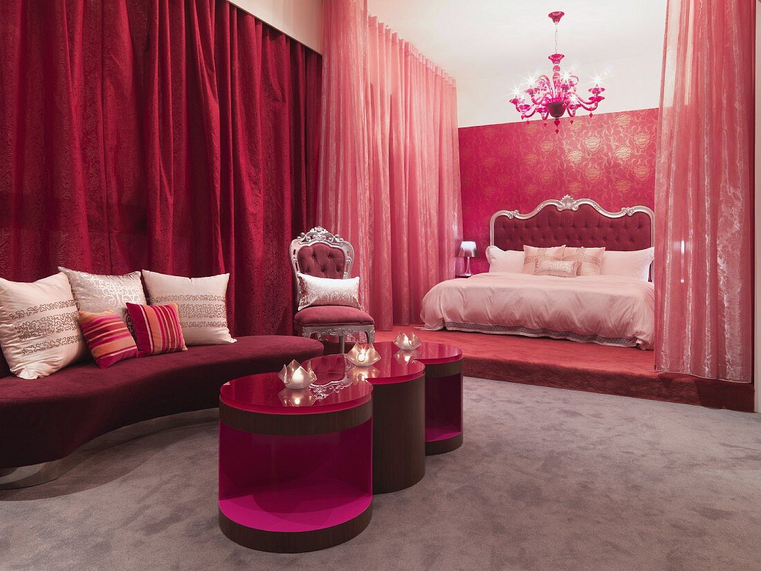 Neobarocker Schlafraum in Rot mit modernen Beistelltischen vor Bett auf Podest und geschlossenen Vorhängen