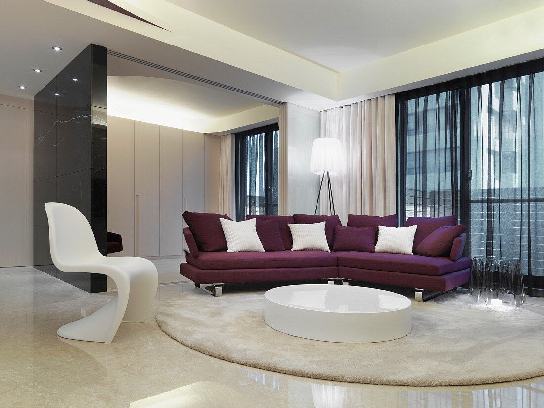 Eleganter Wohnraum mit Klassikerstuhl und modernem Sofa in Violett vor rundem Bodenmöbel auf Teppich