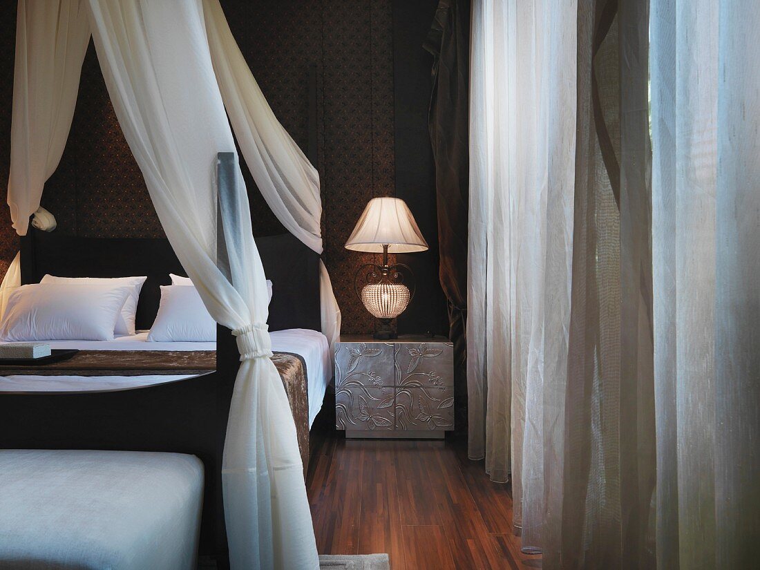 Elegantes Himmelbett mit weißem Vorhang neben Nachttisch und Beleuchtung im Retrostil