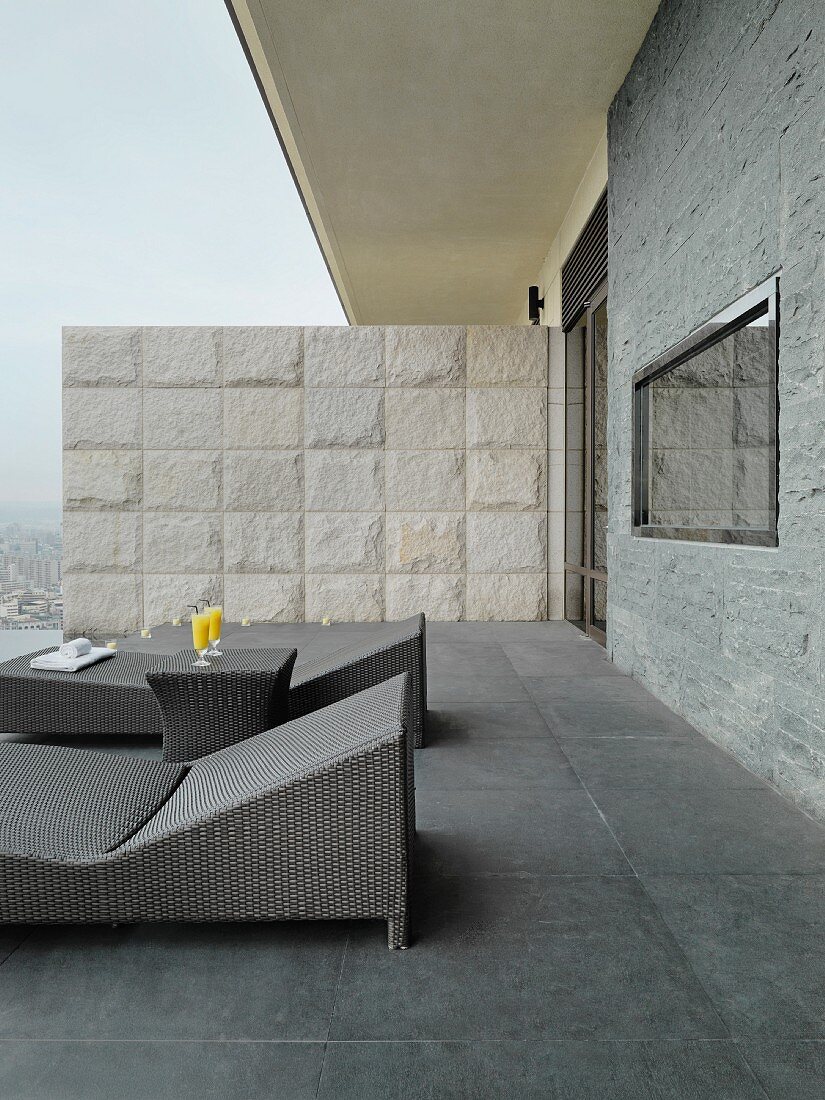 Modern outdoor loungers on roof terrace in various shades of grey with stone partition
